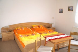 Ein Einzelbett mit Holz Kopfteil, ein Nachttisch mit Lampe, ein Sessel und ein kleiner Tisch mit Tischdecke.