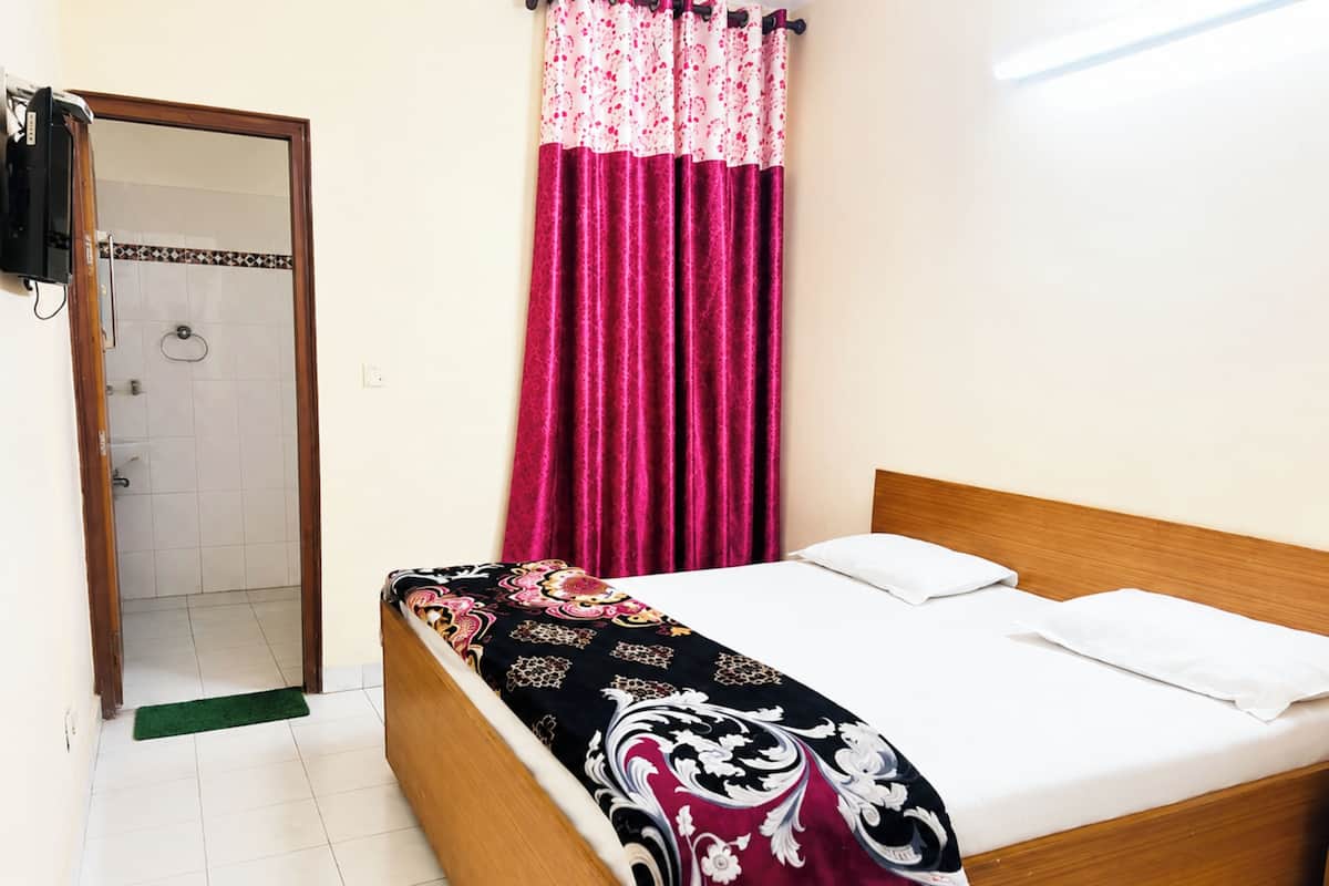 Quarto com cama, cabeceira de madeira, porta de banheiro e cortina de chuveiro.