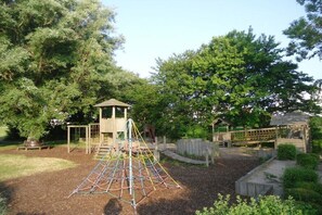 Ein Spielplatz mit Klettergeräten, einem hölzernen Spielhäuschen und einem umzäunten Bereich.