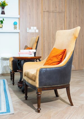 A room with a large armchair, a small table with books, a blue and white striped rug, and a wooden floor.