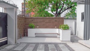 A modern outdoor seating area with a bench, potted plants, and a tiled pathway. - 3 beds Villa with BBQ grill and very fast wifi (Douala)