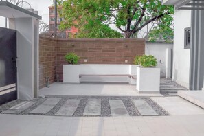 A modern outdoor seating area with a bench, potted plants, and a tiled pathway.