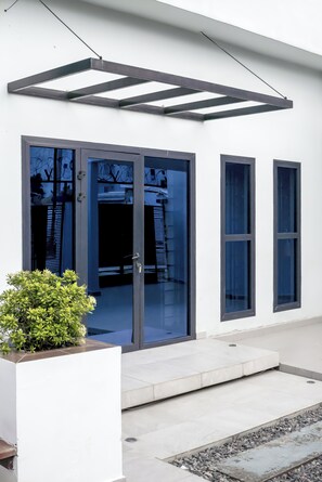 Un edificio moderno con amplias puertas de vidrio, un pequeño jardín y una estructura metálica sobre la entrada.