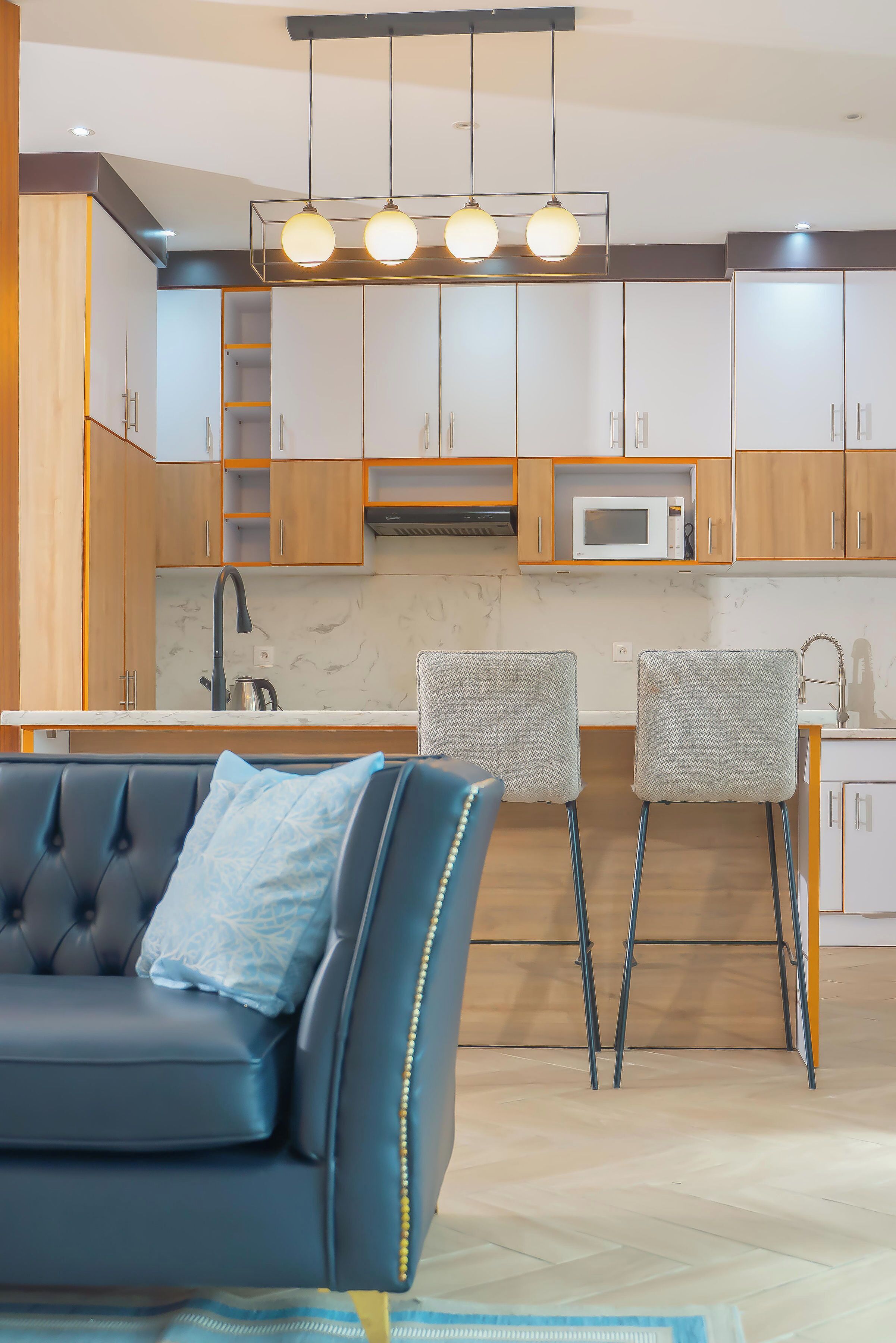 A modern kitchen with wooden cabinets, a microwave, and a black sofa with a blue pillow.