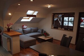Un espace de vie de style loft comprenant un canapé, une table à manger et des chaises, une lucarne et une fenêtre décorée pour Noël (« XMAS »).
