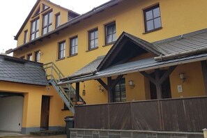 Ein gelbes Gebäude mit einer Treppe, die zu einem überdachten Bereich, einer Garage und einer Steinmauer führt.