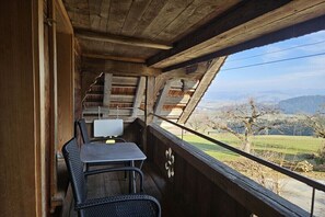 Un balcon en bois, agrémenté d’une table et de chaises, qui offre une vue sur un paysage composé d’arbres et de collines.