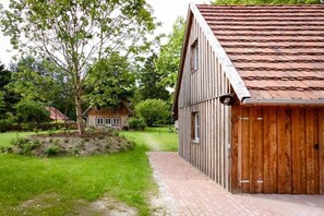 Ein hölzernes Bauernhaus mit rotem Dach, einem Ziegelweg und einem kleinen Haus im Hintergrund.
