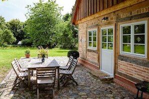Ein Backsteinhaus mit einer Holzterrasse, einer Steinterrasse und einem Tisch mit Stühlen.