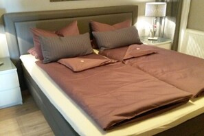 A neatly made bed with a brown bedspread and pillows, a bedside table with a lamp, and a nightstand with a drawer. - Holiday apartment with 2 bedrooms (Otterndorf)