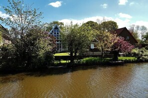 A riverside view with a house, a bridge, and a tree with pink blossoms. - Holiday apartment with 2 bedrooms (Otterndorf)