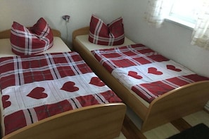 Two single beds with plaid bedding and heart-patterned pillows in a room with a window and a wall socket. - Lake view - Varchentin (Varchentin)
