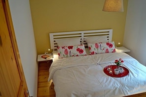 Ein ordentlich bezogenes Bett mit Blumenmuster, ein Nachttisch mit Lampe und ein Tablett mit Tassen und einer Kerze auf dem Bett.