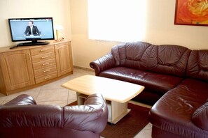 Ein Wohnzimmer mit einer Ledersofa, einem Holzkasten, einem Fernseher und einem kleinen Tisch.