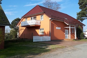 A two-story building with a red roof, a balcony, and a white picket fence. - Holiday apartment with 1 bedroom (Ostseebad Binz)