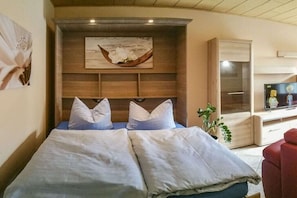 A bedroom with a bed, pillows, a wooden headboard, a wall-mounted artwork, a potted plant, and a TV. - Holiday apartment with 1 bedroom (Ostseebad Binz)