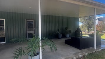 A covered patio area with potted plants, a black outdoor seating area, and a view of the surrounding landscape.