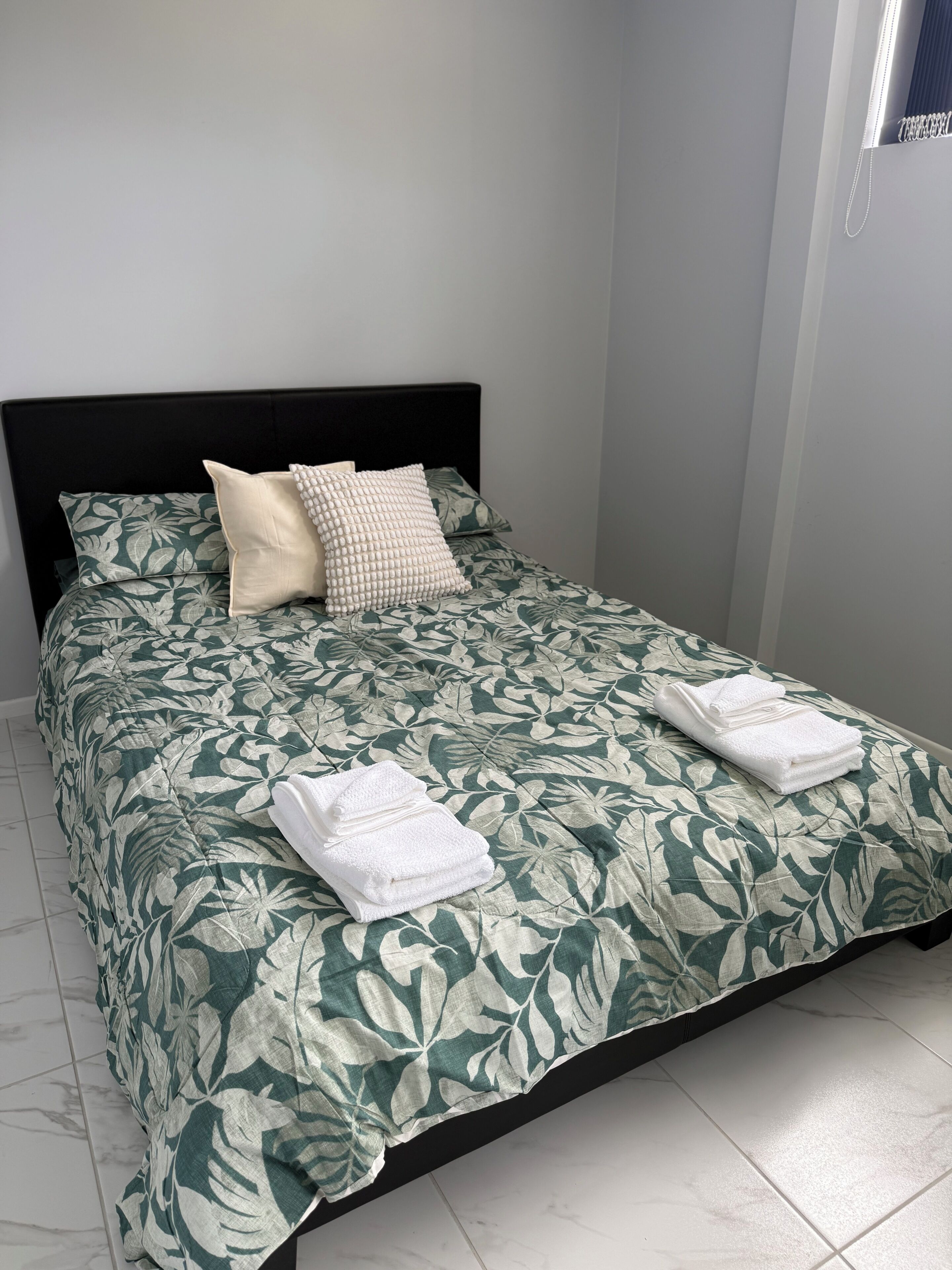 A neatly made bed with a floral bedspread, a black headboard, and two folded towels on the bed.