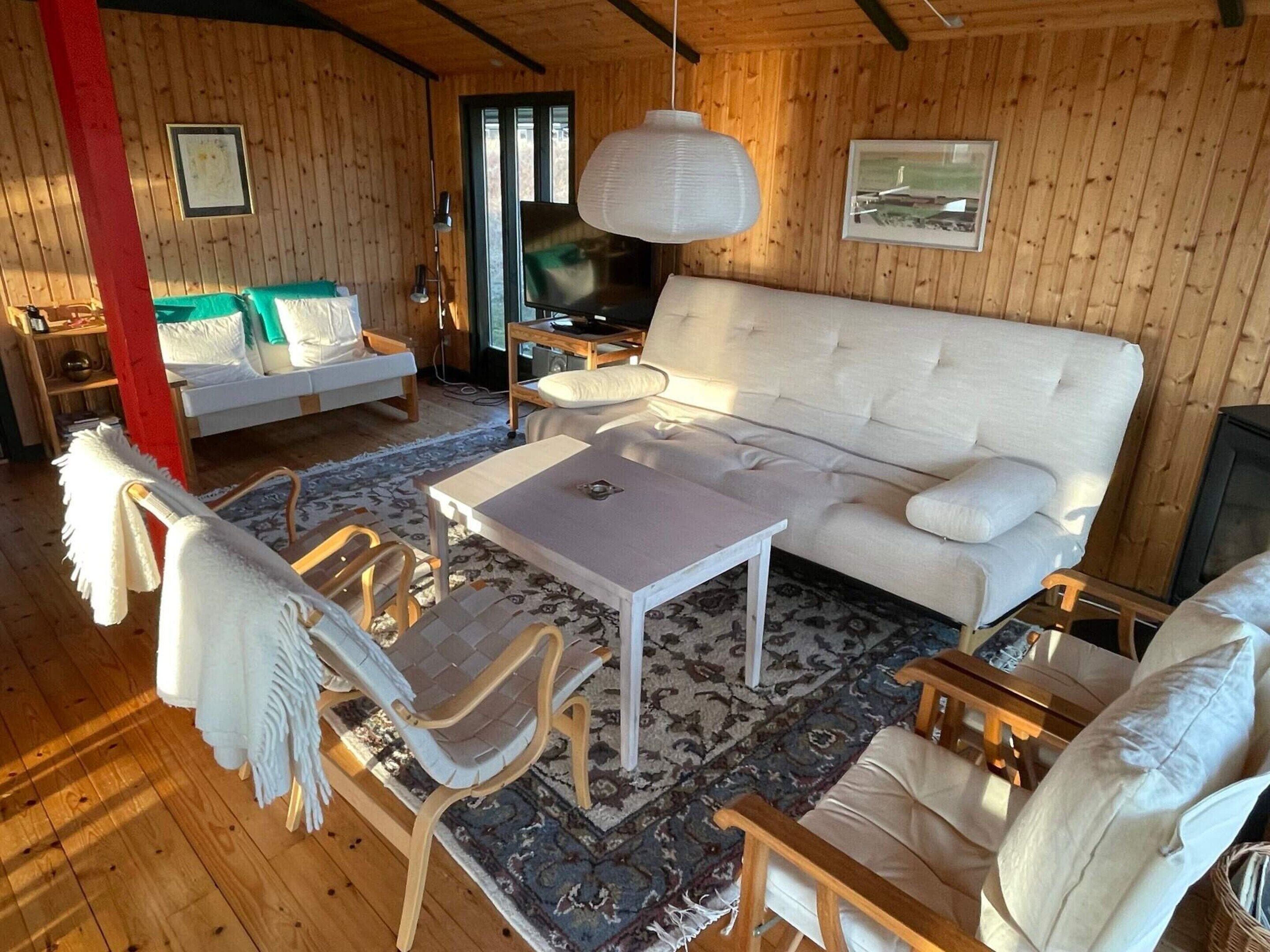 A cozy room with a sofa, a table, and chairs, wooden walls, and a television.