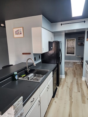 A modern kitchen with a black refrigerator, white cabinets, a stainless steel sink, and a skylight.