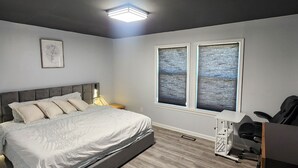 Ein Schlafzimmer mit Bett, Nachttisch, Schreibtisch, Stuhl, Fenster und Deckenleuchte.