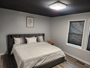 A bedroom with a bed, a nightstand, a window with blinds, and a ceiling light fixture.