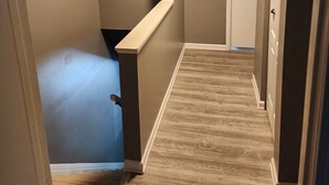 Ein schmaler Korridor mit Holzboden, beigen Wänden und einer weißen Tür am Ende.