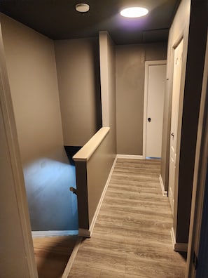 A narrow hallway with a wooden floor, beige walls, and a white door at the end.