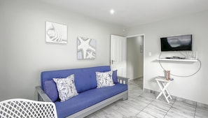 A modern living room with a blue sofa, two wall-mounted artworks, a television on a stand, and a door leading to another room. - Villa Du-baai 1 Luxury Apartment (Mossel Bay)