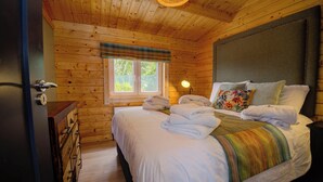 Una habitación de cabaña de madera con una cama, un ventanal y una lámpara.