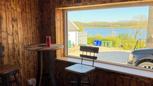 Una habitación con paredes de madera, una ventana con vistas a un lago, una mesa, dos sillas y una taza roja.
