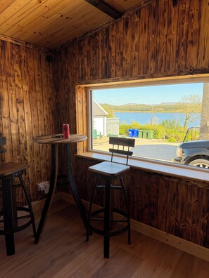 A room with wooden walls, a window with a view of a lake, a table, two chairs, and a red cup.