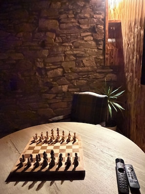 A wooden chessboard on a table with a stone wall and a wooden cabinet in the background.