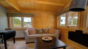 Una habitación acogedora con techo de madera, un sofá con cojines de colores, una mesa con un control remoto y una ventana que da a zonas verdes.