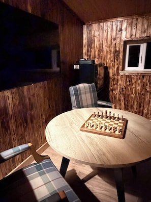 A wooden interior with a round table set for a game, plaid chairs, and a window.