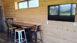 Una habitación con paneles de madera, una mesa de comedor, sillas, un televisor montado en la pared y un equipo de aire acondicionado.