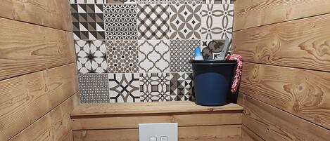 A small, wooden-paneled bathroom with a white toilet, a wall-mounted flush handle, and a patterned tile backsplash.