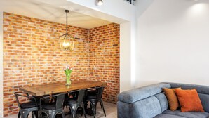 Un comedor con pared de ladrillo, mesa de madera, sillas negras y una lámpara colgante.