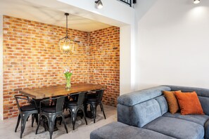 Un coin repas avec un mur en briques, une table en bois, des chaises noires et un luminaire suspendu.