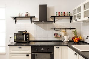 Eine moderne Küche mit Mikrowelle, Backofen, schwarzer Dunstabzugshaube, weißen Schränken und einer Obstschale auf der Arbeitsplatte.