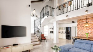 Un salón espacioso con televisión de pantalla plana, un sofá, una mesa de centro y una escalera que lleva a un nivel superior.