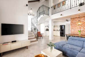 Ein geräumiger Wohnbereich mit Flachbildfernseher, einer Couch, einem Couchtisch und einer Treppe, die zu einer oberen Ebene führt.