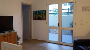 En stue med et fjernsyn på et træskab, en dør der fører til en balkon, og et billede på væggen.