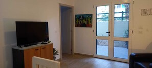 A living room with a television on a wooden cabinet, a door leading to a balcony, and a painting on the wall. - Salty Holiday Apartment in The Branco Sea condominium (Santa Maria)