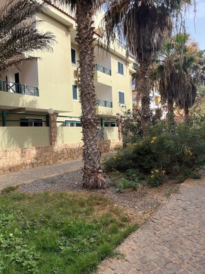 A building with a stone wall, a paved pathway, and palm trees. - Salty Holiday Apartment in The Branco Sea condominium (Santa Maria)