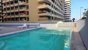 Una piscina con due poltrone bianche, circondata da un muretto basso e un edificio con numerosi balconi.