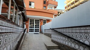 Un vialetto stretto conduce all'ingresso di un edificio, con un muro rivestito di piastrelle su un lato e una ringhiera metallica sull'altro.