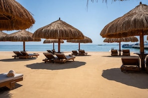 Una playa con tumbonas y sombrillas de paja.