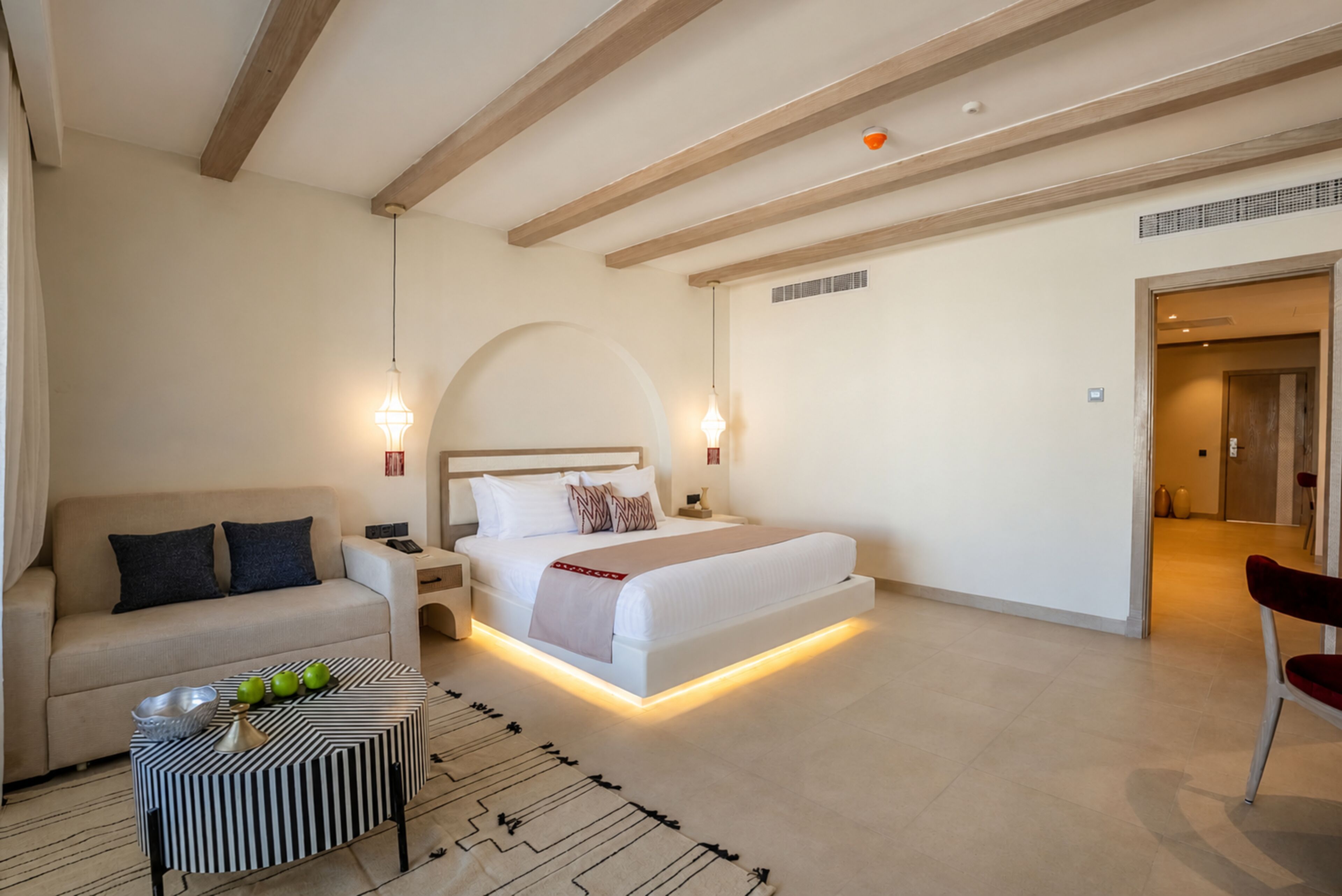 Un dormitorio moderno con cama, sofá, mesita de noche y una pequeña mesa con objetos decorativos.