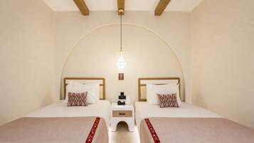 Habitación de hotel con dos camas, una mesita de noche pequeña con un teléfono y una lámpara colgante.